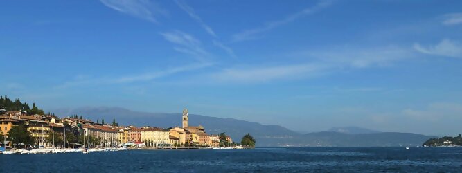 Trip Urlaub beliebte Urlaubsziele am Gardasee -  Mit einer Fläche von 370 km² ist der Gardasee der größte See Italiens. Es liegt am Fuße der Alpen und erstreckt sich über drei Staaten: Lombardei, Venetien und Trentino. Die maximale Tiefe des Sees beträgt 346 m, er hat eine längliche Form und sein nördliches Ende ist sehr schmal. Dort ist der See von den Bergen der Gruppo di Baldo umgeben. Du trittst aus deinem gemütlichen Hotelzimmer und es begrüßt dich die warme italienische Sonne. Du blickst auf den atemberaubenden Gardasee, der in zahlreichen Blautönen schimmert - von tiefem Dunkelblau bis zu funkelndem Türkis. Majestätische Berge umgeben dich, während die Brise sanft deine Haut streichelt und der Duft von blühenden Zitronenbäumen deine Nase kitzelt. Du schlenderst die malerischen, engen Gassen entlang, vorbei an farbenfrohen, blumengeschmückten Häusern. Vereinzelt unterbricht das fröhliche Lachen der Einheimischen die friedvolle Stille. Du fühlst dich wie in einem Traum, der nicht enden will. Jeder Schritt führt dich zu neuen Entdeckungen und Abenteuern. Du probierst die köstliche italienische Küche mit ihren frischen Zutaten und verführerischen Aromen. Die Sonne geht langsam unter und taucht den Himmel in ein leuchtendes Orange-rot - ein spektakulärer Anblick.